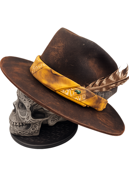 Brown hat with yellow band and feather on a skull-shaped stand against a white background